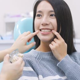 A woman pointing at her smile at a dental office.