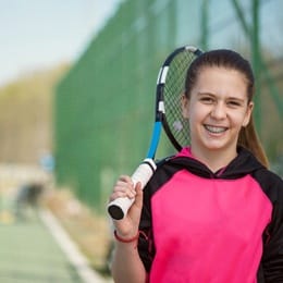 A young girl holding a tennis racket and wearing braces