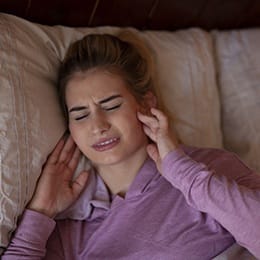 A young female lying in bed and holding both sides of her jaw in pain because of bruxism