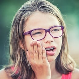 Young girl with braces holding cheek in pain