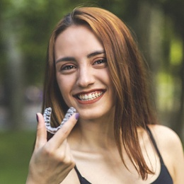 A young female teenager holding an aligner to straighten her smile as part of her treatment with Invisalign in Huntington
