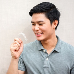 A male teenager wearing a gray shirt and holding a clear Invisalign aligner