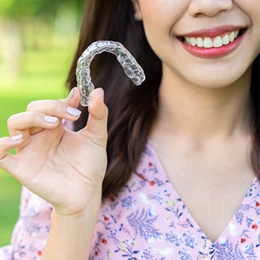 An up-close image of a young female holding an Invisalign aligner in her right hand