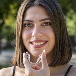 A young female with brown hair holding an Invisalign aligner in her hand and preparing to insert it into her mouth