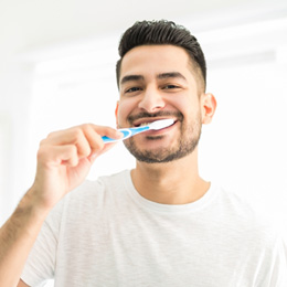 Man smiling while brushing his teeth