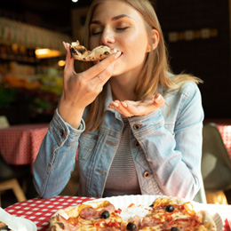 Woman enjoying slice of pizza in restaurant