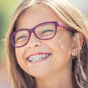 A young girl wearing purple glasses and metal braces smiling after seeing her orthodontist in Huntington