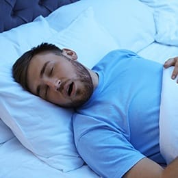 A young man asleep in bed with his mouth open and snoring