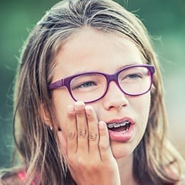 Teen girl with braces holding cheek in pain