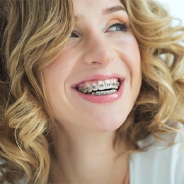 A young female with blonde, curly hair and smiling while showing off her metal braces