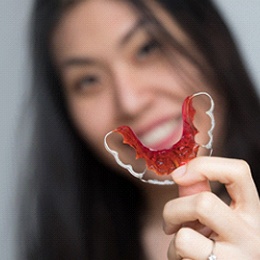 A young female with long, dark hair holding a red-colored, metal retainer