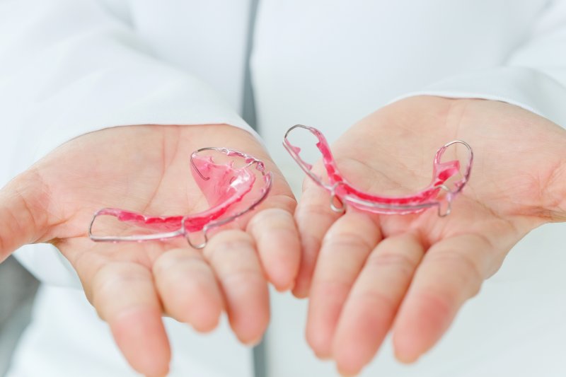 a person holding two dental retainers in the palms of their hands