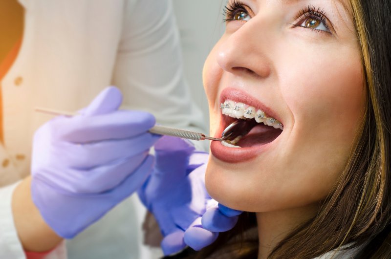 Dentist wearing blue latex gloves and holding dental tool up to girl with braces
